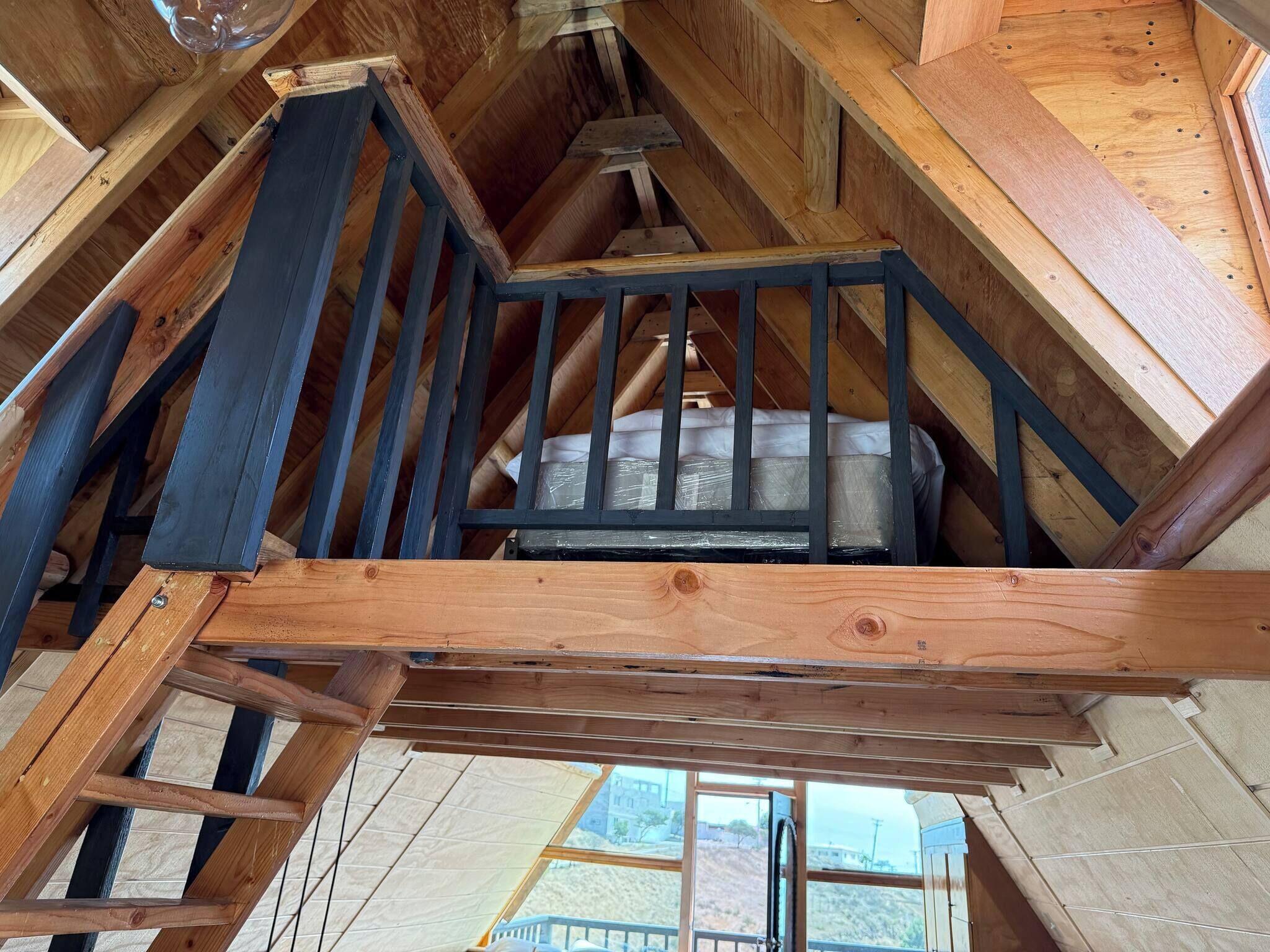 A wooden staircase with a black railing leading to a loft area with a mattress.