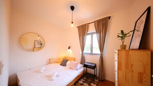 A neatly made bed with a wooden headboard, a small bedside table, a mirror on the wall, a window with curtains, and a wooden cabinet. - Tinj Rustic Holiday Home for 8 (Benkovac)