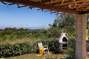 Ein rustikaler Außenbereich mit Holzpergola, Steinpfeiler und Pizzaofen.