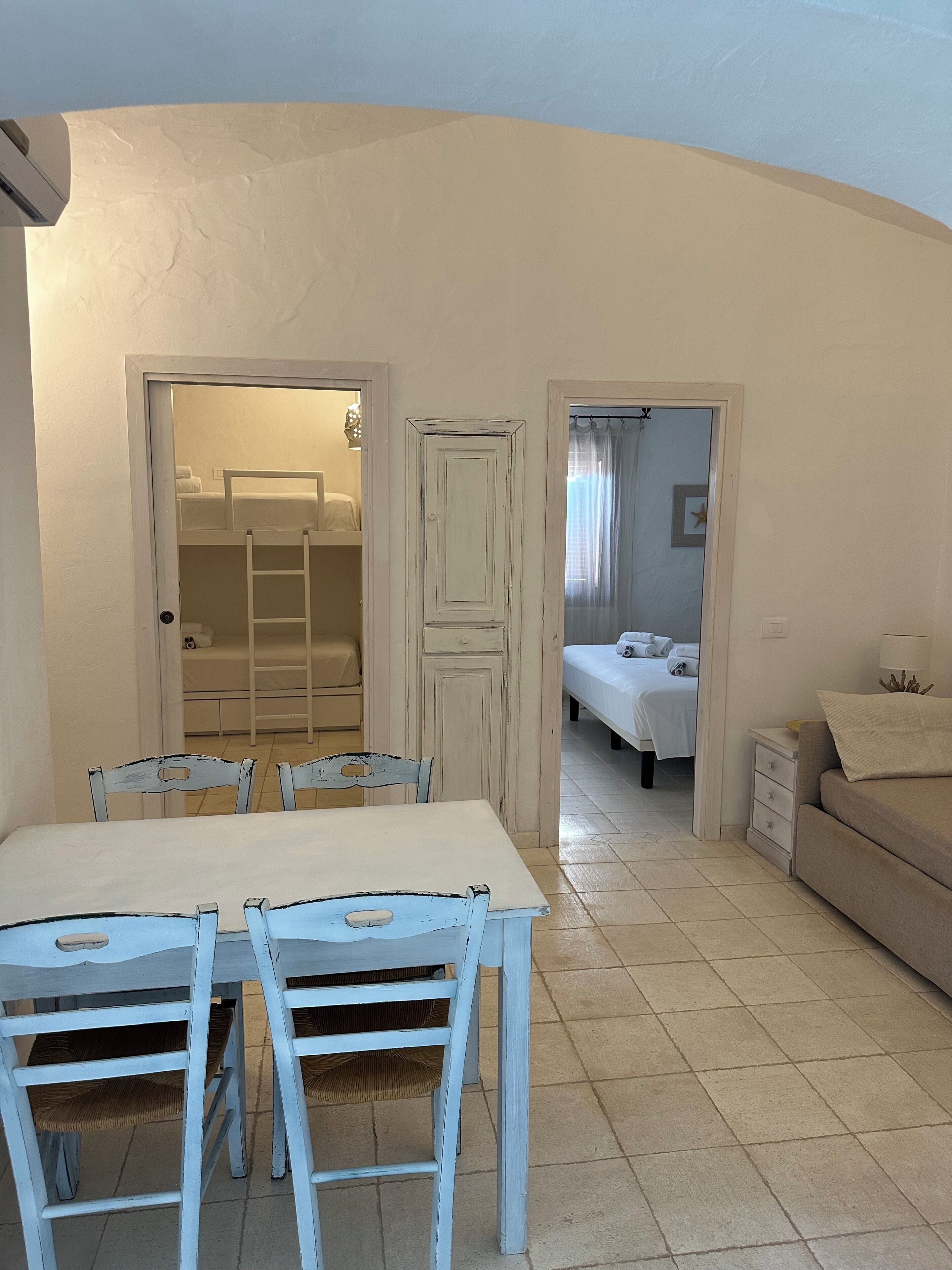 A room with a dining table and chairs, a wardrobe, a bed, and a nightstand.