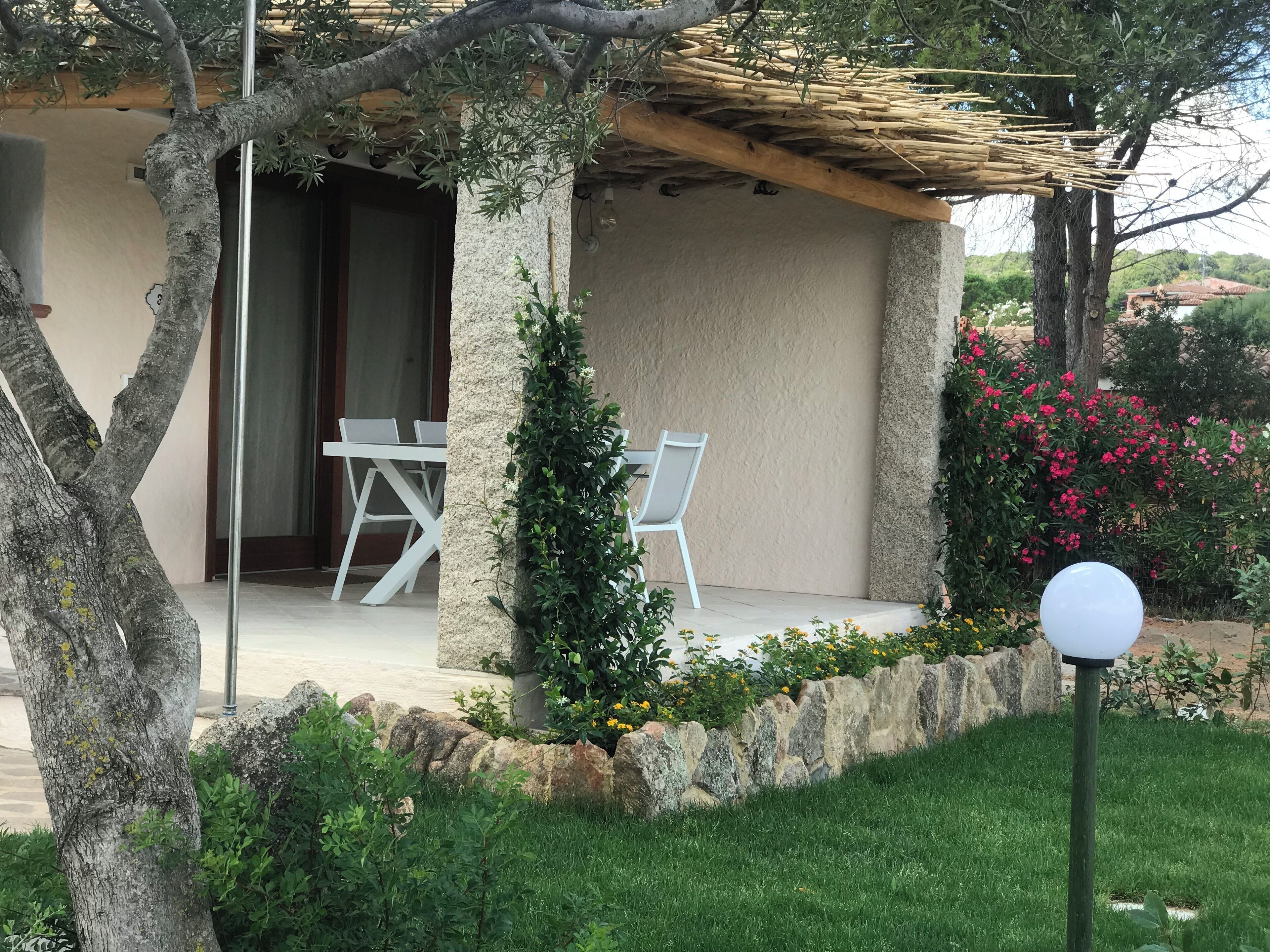 A covered outdoor seating area with two white chairs, a stone wall, and a lamp post.