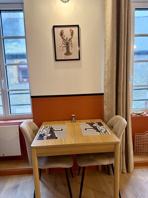 A dining table with two chairs, a framed picture on the wall, and a window with curtains.