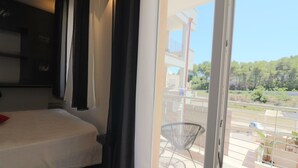 A hotel room with a bed, a window with curtains, and a view of a balcony with a chair and greenery outside. - Vacation Home in Otranto with 1 bedrooms sleeps 2 (Otranto)