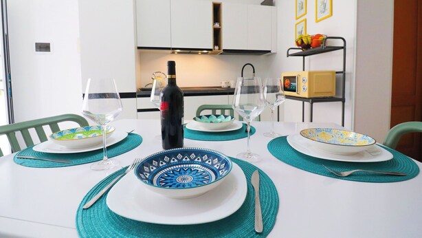 Una mesa de comedor dispuesta con platos azules y blancos, una botella de vino y manteles individuales color verde azulado.