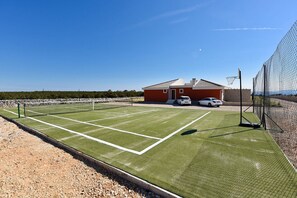 En tennisbana med nät, en röd byggnad och en bil som står parkerad i närheten.