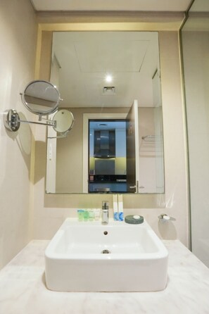 A bathroom with a white sink, a round mirror, and a glass shower enclosure. - Stylish Studio with Balcony  DAMAC Prive Tower A (Dubai)
