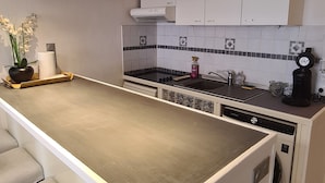 A modern kitchen with white cabinets, a central island with bar stools, a dishwasher, and a coffee maker. - Large Studio very well located! 100m tramway, 5 minutes downtown, 10min beach! (Nice)