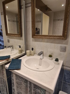 Ein Badezimmer mit einem weißen Waschbecken, zwei Spiegeln mit aufwendigen Rahmen, einem Handtuchhalter und einer kleinen Pflanze.