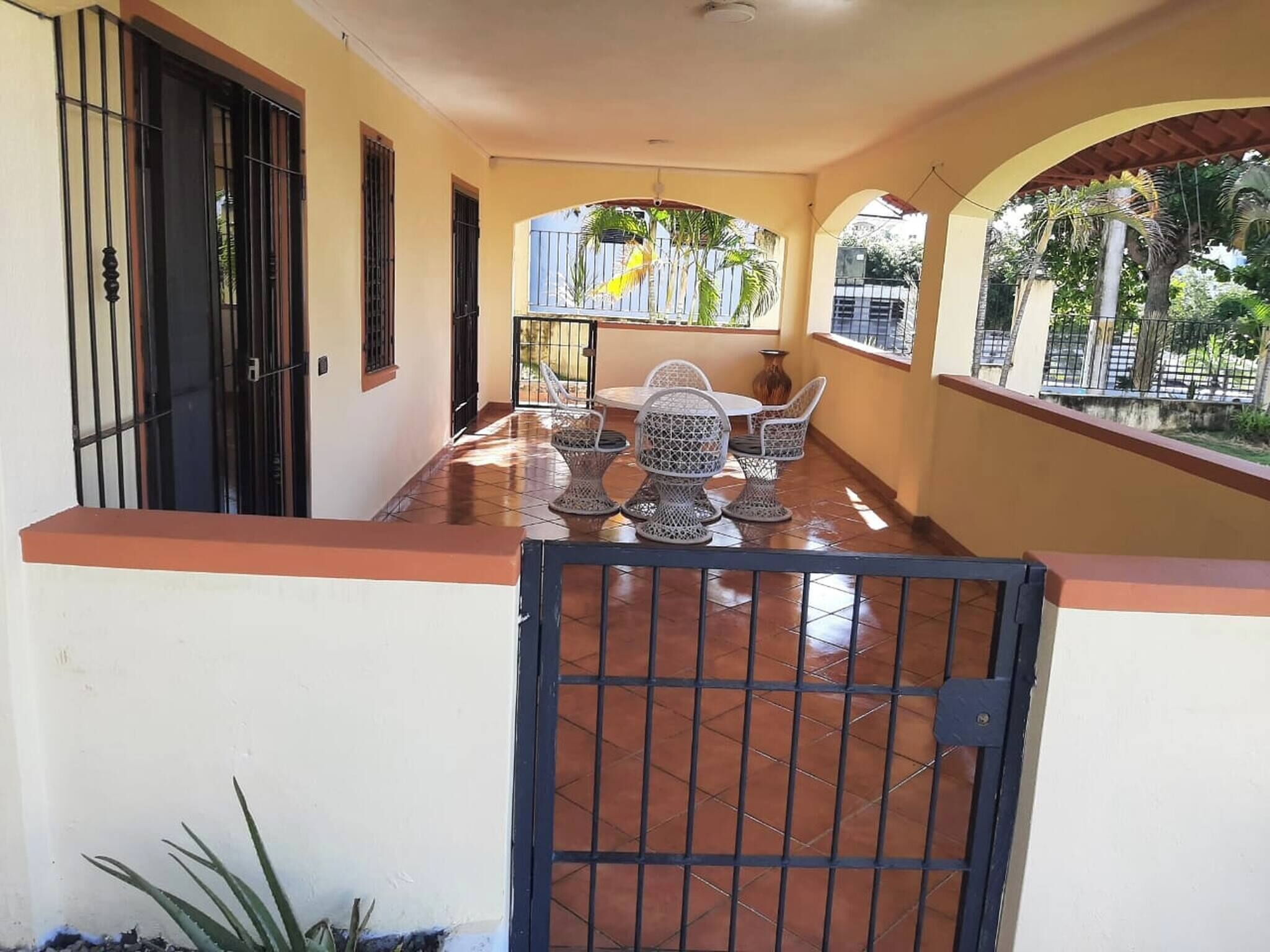 A covered outdoor patio with a tiled floor, a table with chairs, and a gate.