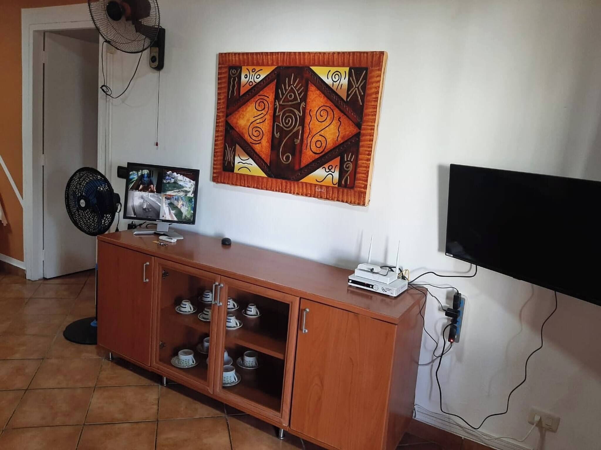 Ein Wohnzimmer mit einem Holzschrank, einem Flachbildfernseher, einem Wandbild und einem Ventilator.