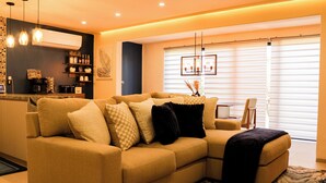 Ein modernes Wohnzimmer mit einem beige farbenen Sofa, einer Kaffeebar und einem Essbereich mit Tisch und Stühlen.