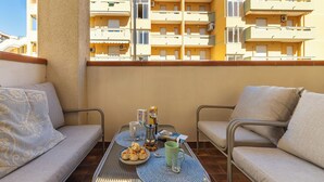 Ein Balkon mit Tisch für zwei Personen, einer Couch und Blick auf ein gelbes Gebäude mit mehreren Balkonen.