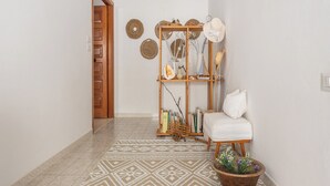 Ein Korridor mit einem gemusterten Teppich, einer Holztür, einem weißen Stuhl, einem kleinen Tisch mit einem Topfpflanzen und einer Holzwand mit Dekorationen.
