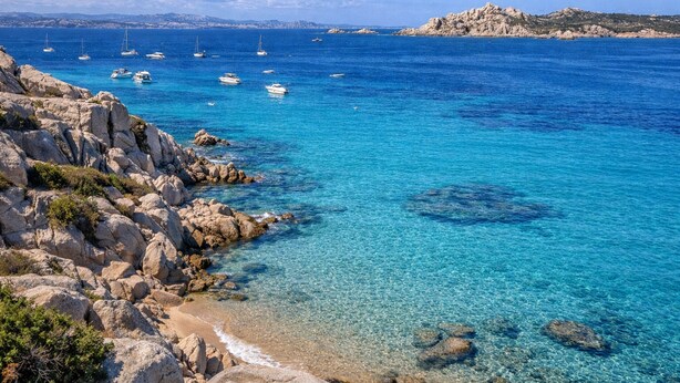 Un paysage côtier avec une eau d’un bleu limpide, des rivages rocheux et des bateaux.