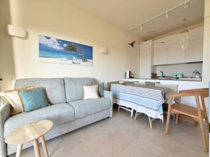 A cozy living room with a grey sofa, a small round table, and a striped tablecloth. A painting of a beach scene hangs on the wall. - Charming accommodation in Palau (Palau)