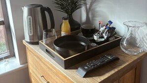 A kitchen counter with a kettle, a plant, a tray with kitchen items, a remote control, and a TV mounted on the wall.