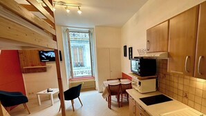 A compact kitchen with wooden cabinets, a microwave, a sink, and a dining area with a table and chairs. - Mezzanine Spa Stay for 4 (La Bourboule)