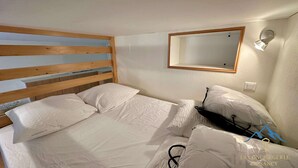 A bedroom with a wooden headboard, a bed with white bedding, a bedside table with a lamp, and a mirror on the wall. - Mezzanine Spa Stay for 4 (La Bourboule)