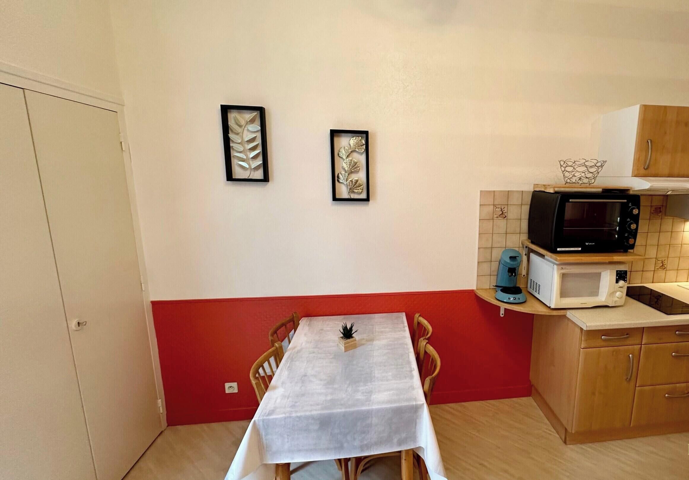 A compact kitchen with a dining table, two framed wall art pieces, and a microwave on a countertop.