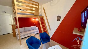 A compact room with a loft bed, a sofa, two chairs, a small table, and a TV. - Mezzanine Spa Stay for 4 (La Bourboule)