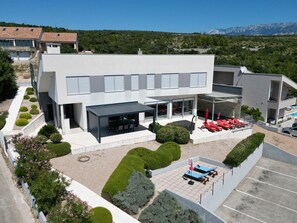 A modern hotel with a covered outdoor seating area, a pool, and a view of mountains in the background. - Charming Villa With Heated Pool (Posedarje)