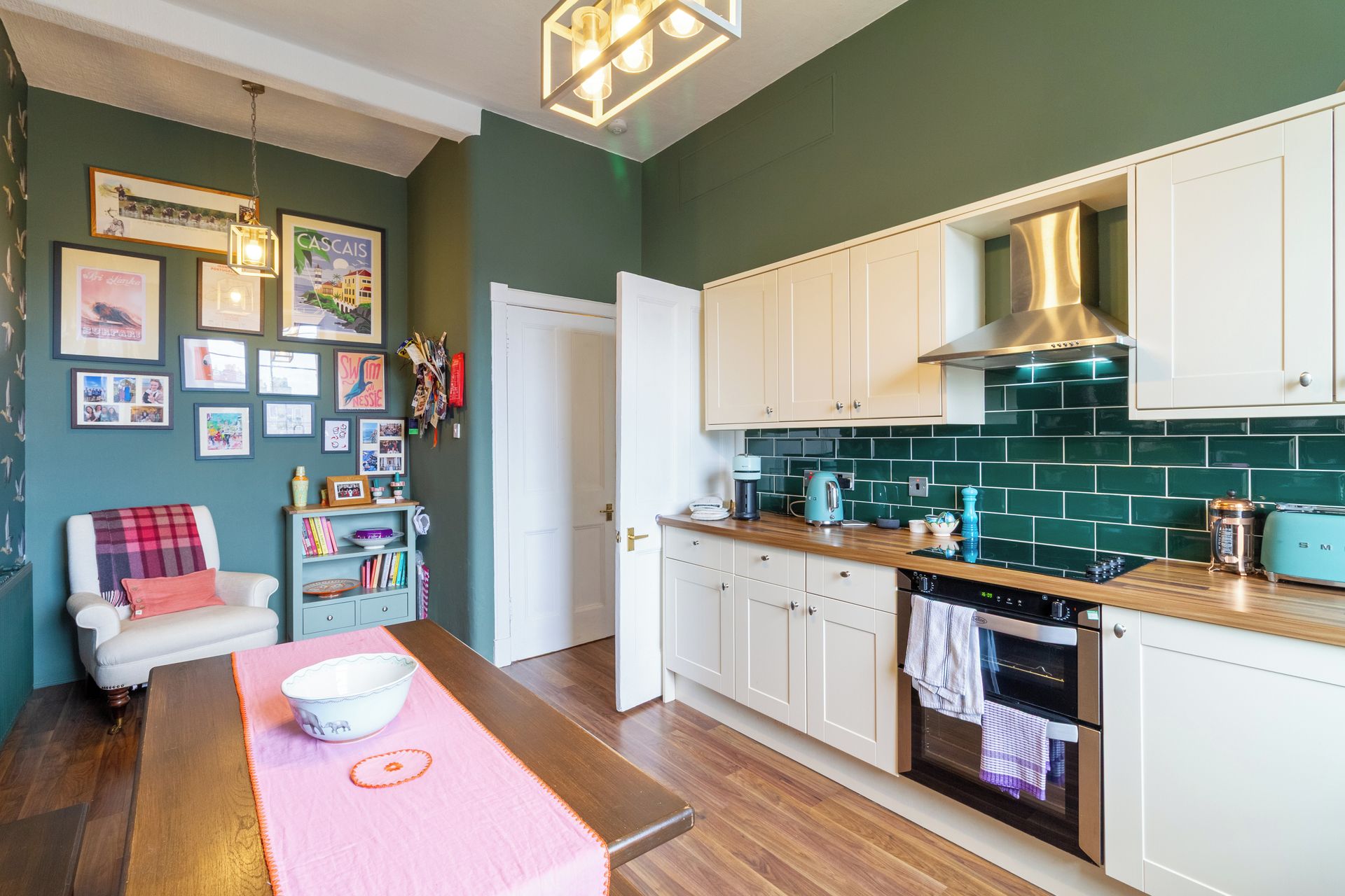 A kitchen with white cabinets, a stainless steel range hood, and a green tiled backsplash.