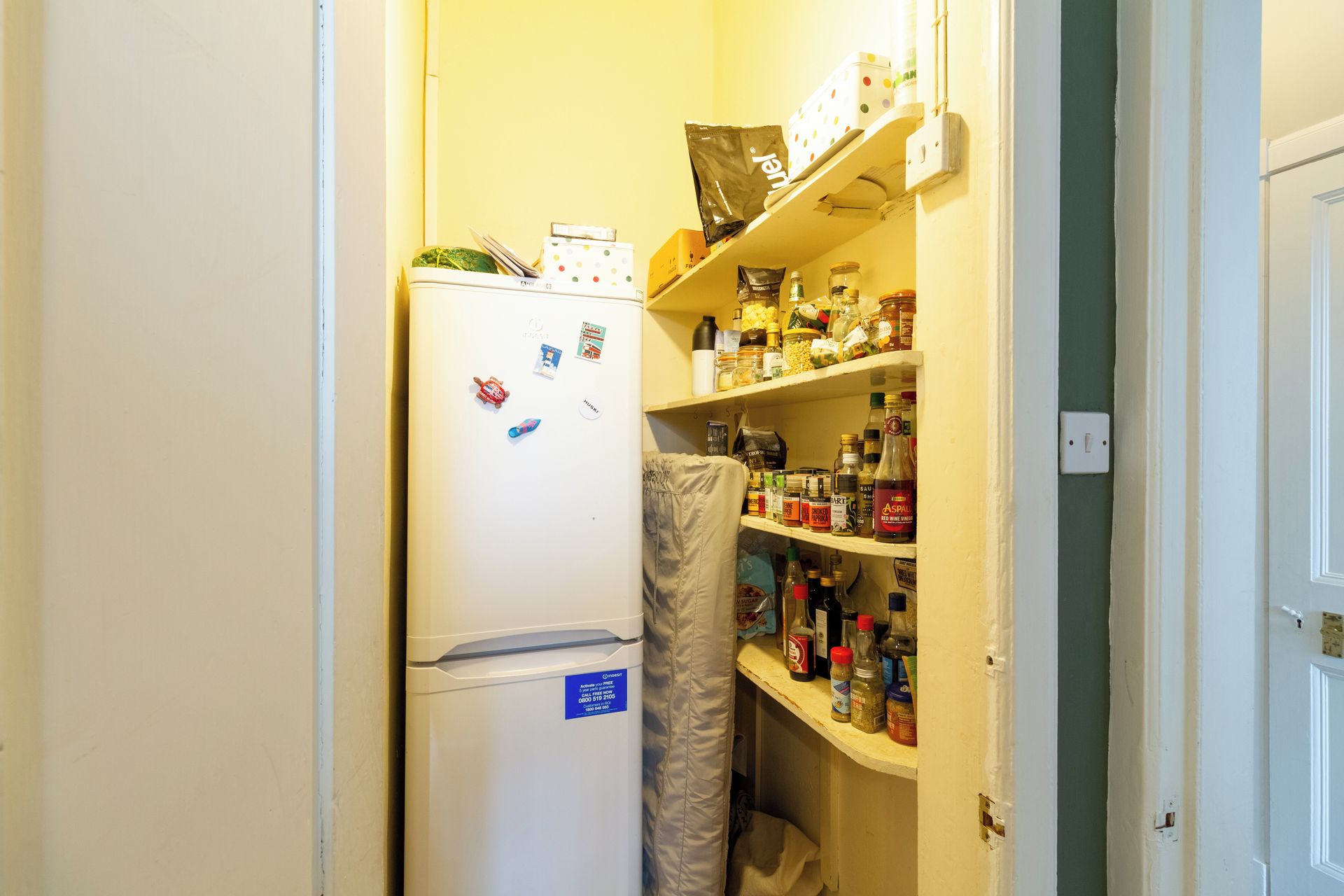 A compact kitchen with a refrigerator, shelves stocked with various food items, and a microwave.