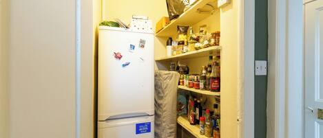 A compact kitchen with a refrigerator, shelves stocked with various food items, and a microwave.
