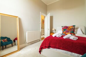 Een hotelkamer met een bed, een grote spiegel, een radiator en een blauwgroene fauteuil.