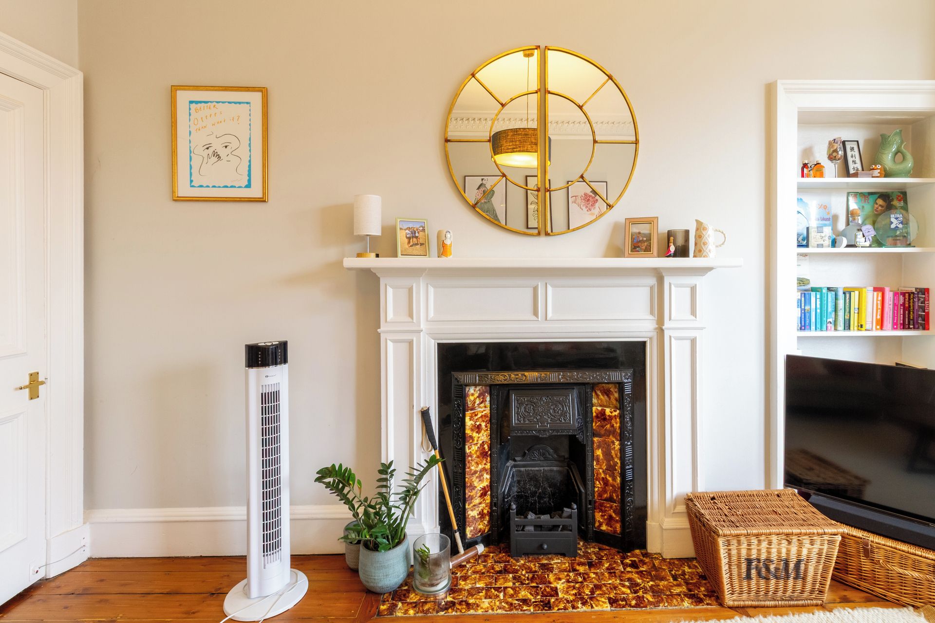 A living room with a fireplace, a large mirror, a bookshelf, and a floor heater.