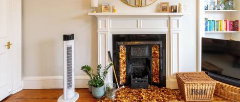 A living room with a fireplace, a large mirror, a bookshelf, and a floor heater.