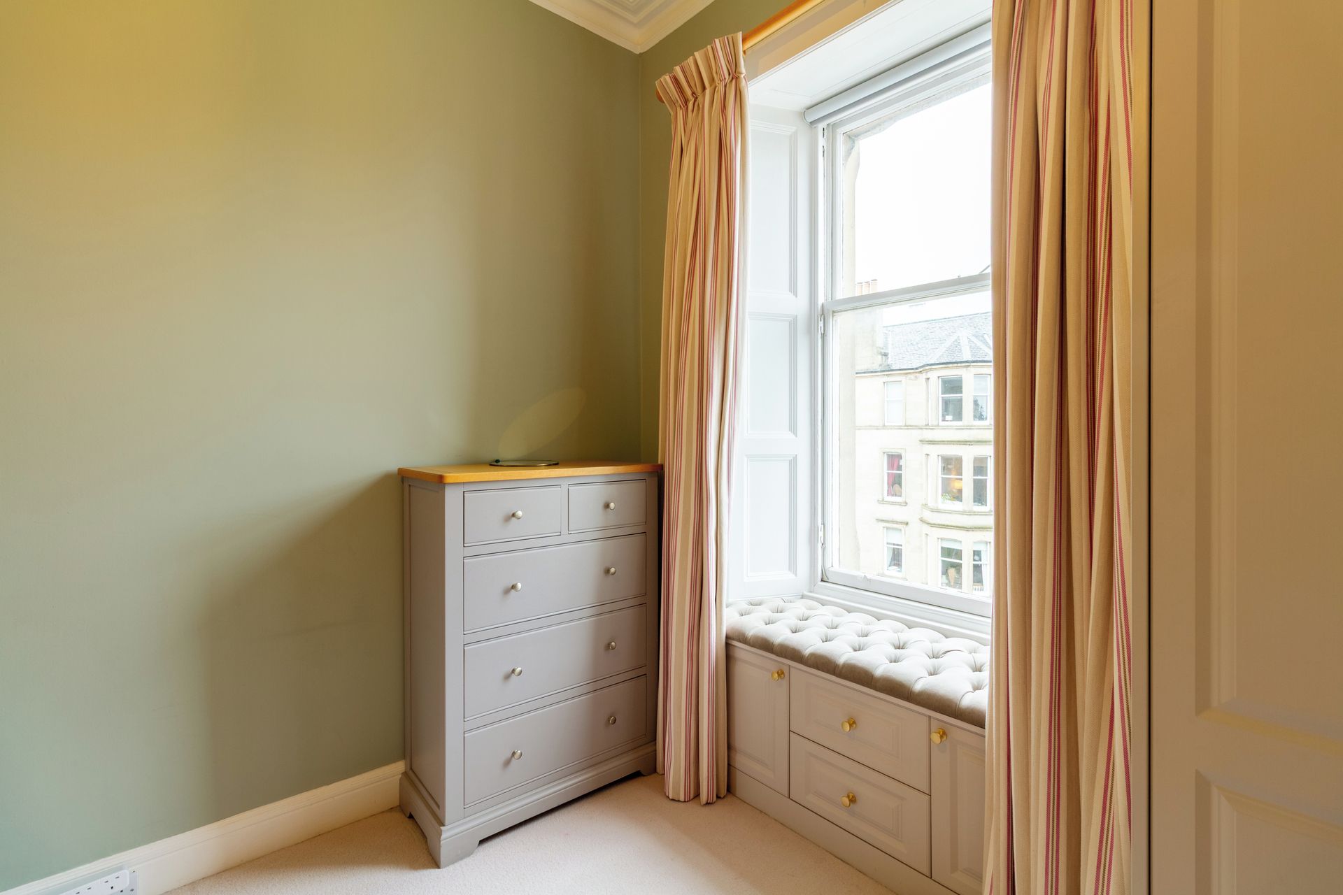 A corner room with a window, a dresser, and a bench.