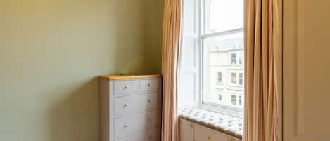 A corner room with a window, a dresser, and a bench.