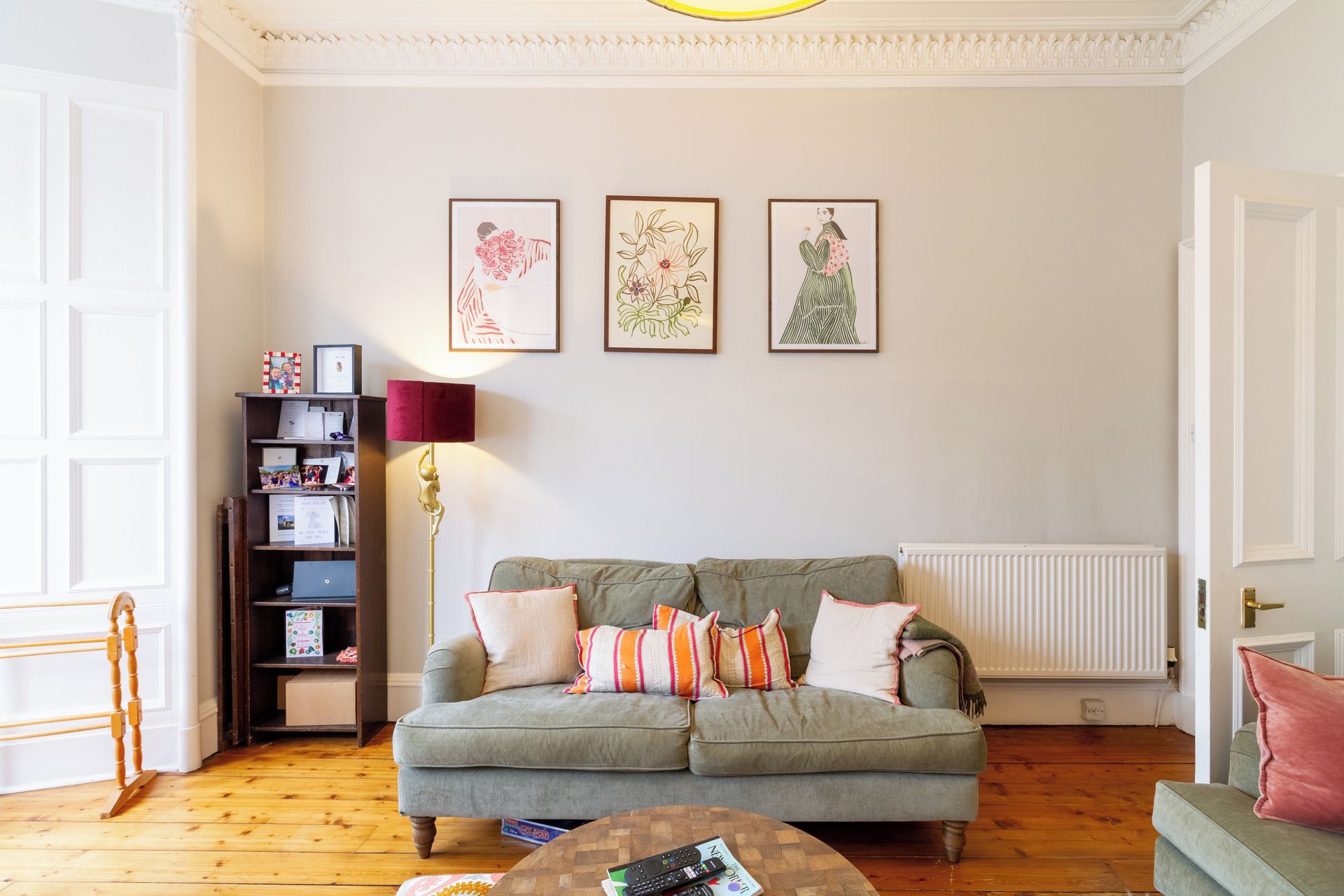 A living room with a grey sofa, a wooden floor, a bookshelf, and three framed artworks on the wall.