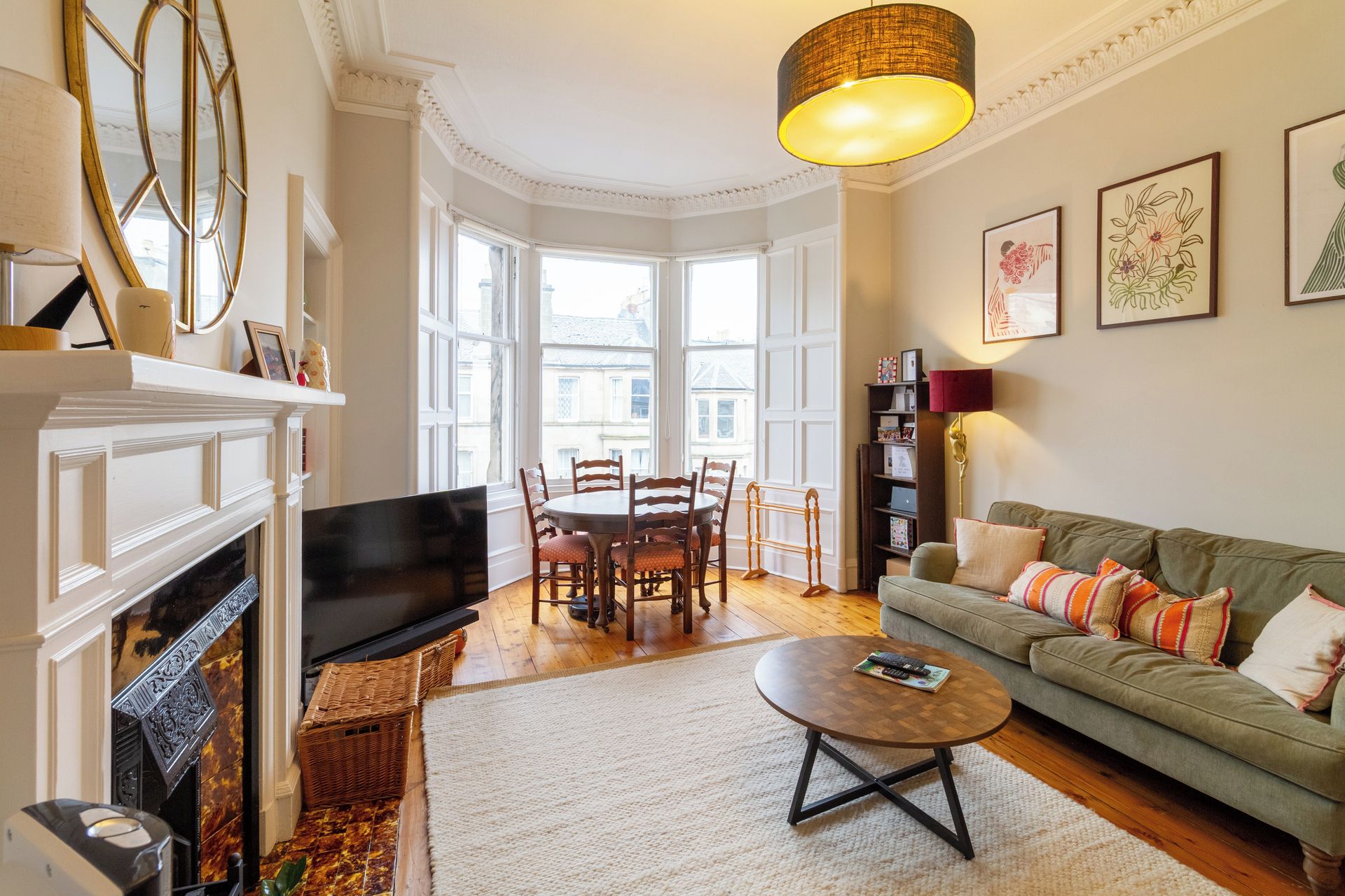 A living room with a fireplace, a green sofa, a dining table with chairs, and a large window.