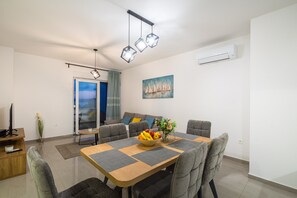 Un soggiorno moderno con zona pranzo, divani grigi, un tavolo da pranzo in legno con una ciotola di frutta e un quadro appeso al muro.