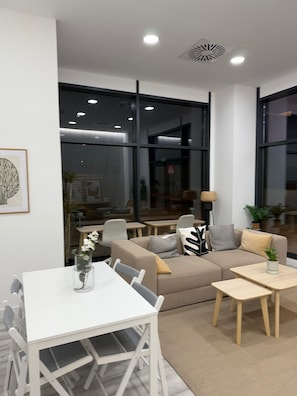 Ein modernes Wohnzimmer mit einem weißen Esstisch, einem beigen Sofa und zwei kleinen Beistelltischen.