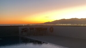 Een zonsondergang uitzicht vanaf een dak terras met een zwembad, bar en verre stadslichten.