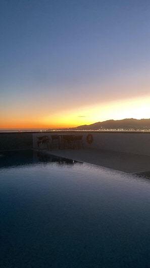 Sonnenuntergangblick von einer Dachterrasse mit Pool, Bar und weiter Stadtansicht.