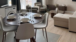 Een moderne woonkamer met een eethoek, een flatscreen televisie aan de muur en stadszicht door grote ramen.