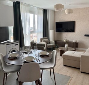 Ein modernes Wohnzimmer mit Essbereich, einem an der Wand befestigten Flachbildfernseher und Blick auf die Stadt durch große Fenster.