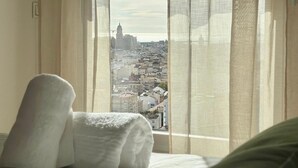 Een hotelkamer met een bed, een raam met dunne gordijnen en uitzicht op een stadsbeeld.