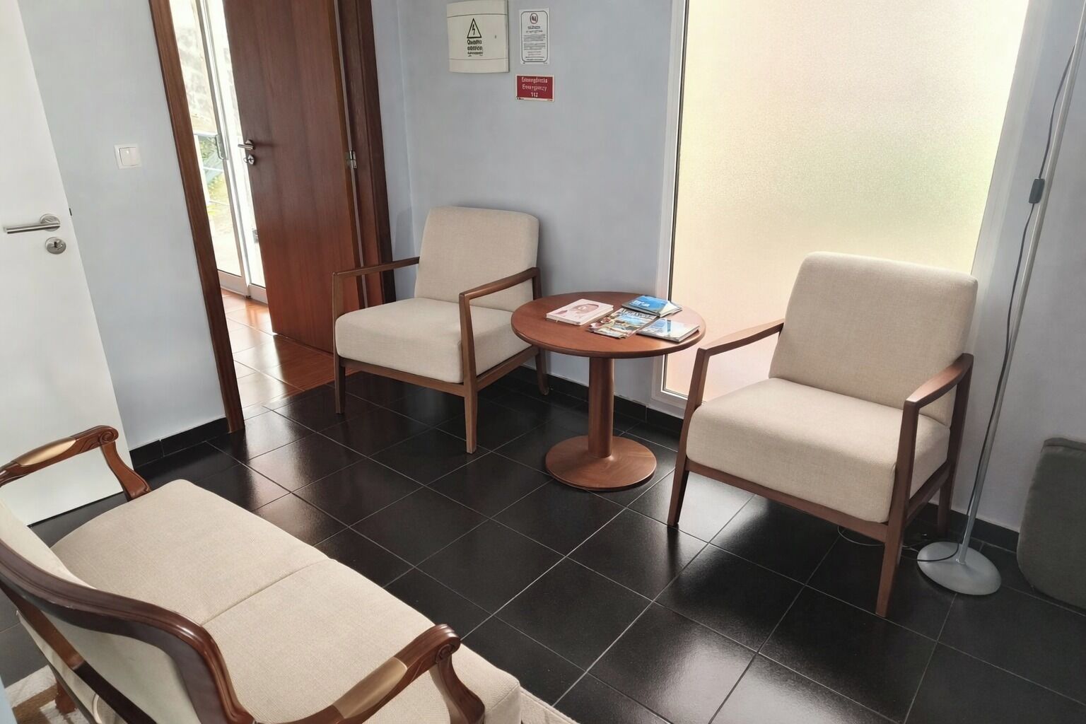 Une chambre d’hôtel avec une chaise en bois, une table ronde sur laquelle sont posés des magazines, et une vue sur l’extérieur par une porte vitrée.