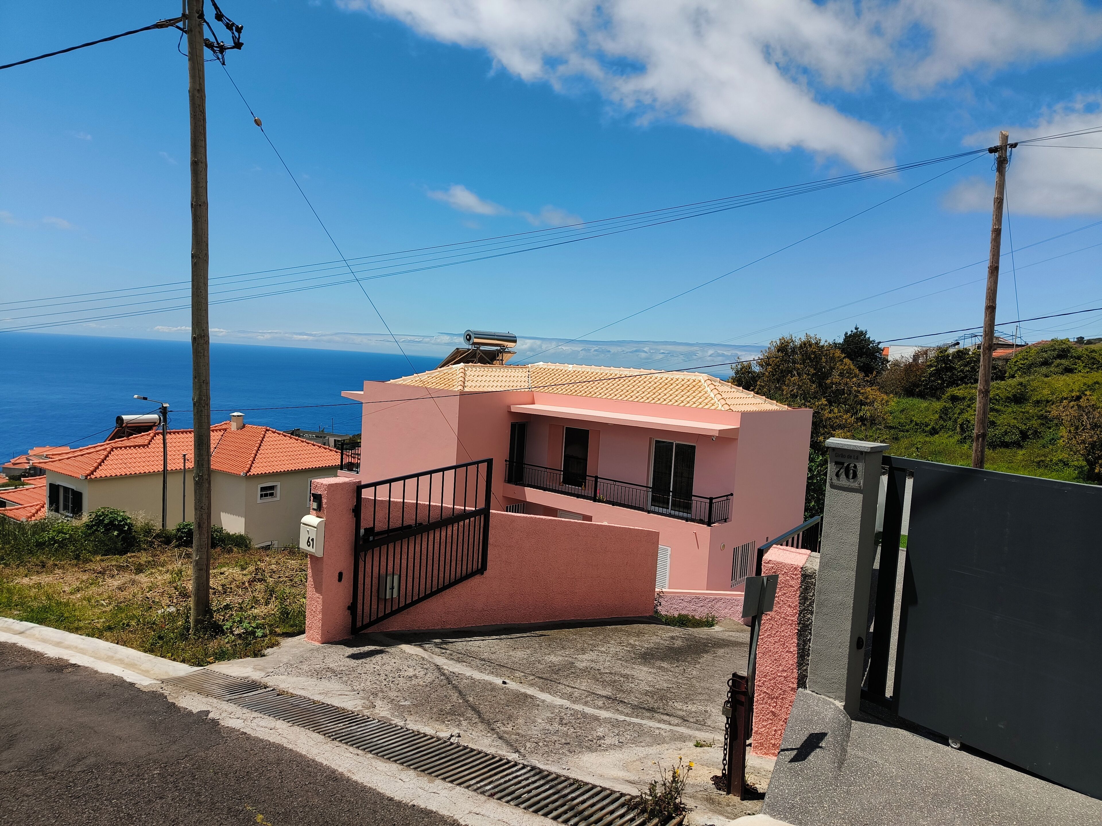 Ein rosafarbenes Gebäude mit Balkon, einem Vorgarten und Blick auf das Meer.