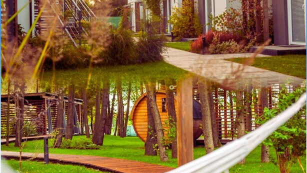 A modern residential area with a wooden cabin-like structure surrounded by trees and a pathway leading to a row of houses. - Baltic Natur Park - Apartament B (Niechorze)