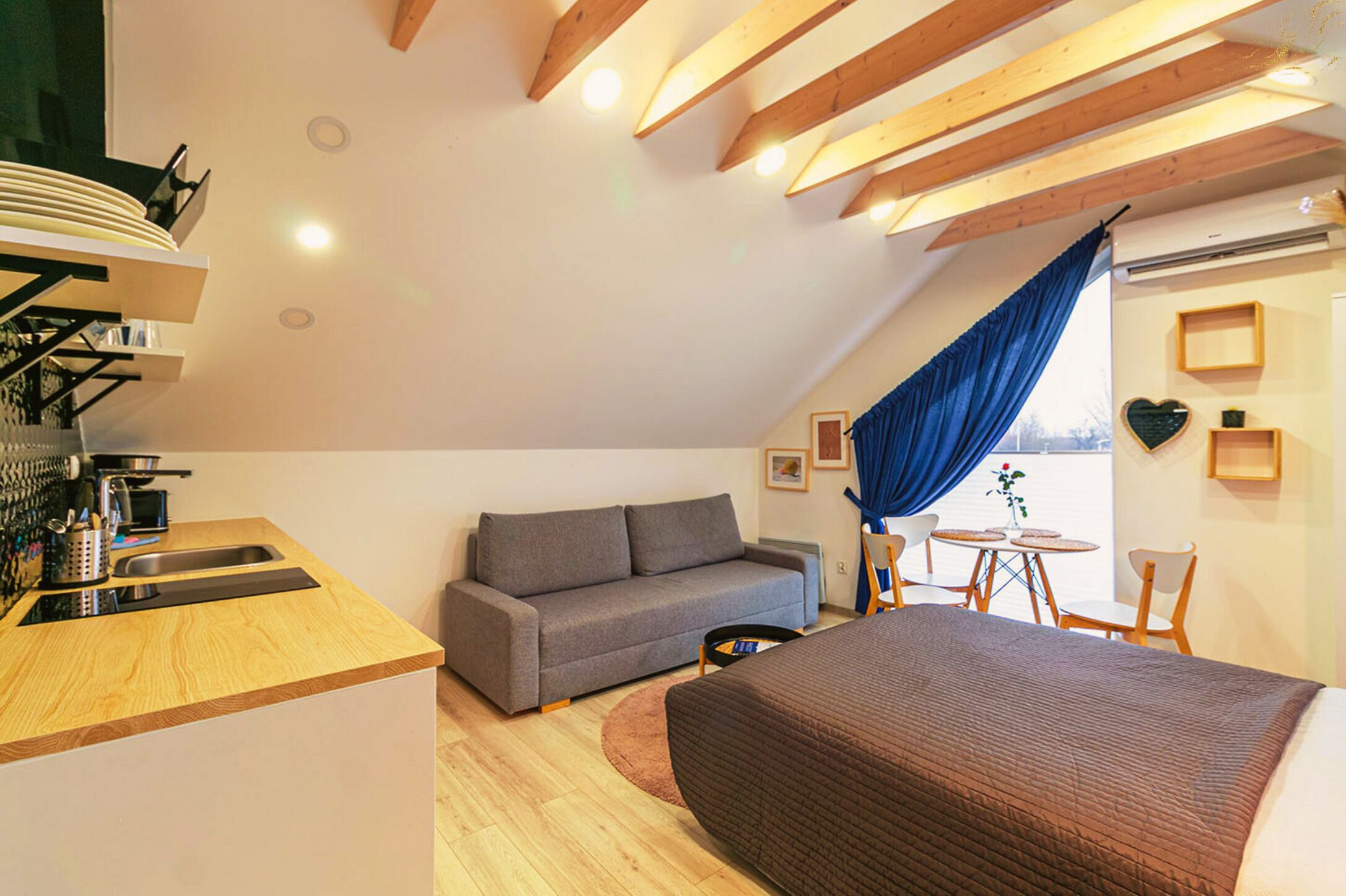 A modern loft bedroom with a sloped ceiling, a sofa, a bed, a dining table, and a kitchen area.