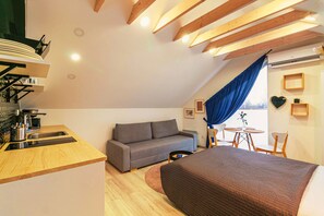 Et moderne loftværelse med skrå vægge, en sofa, en seng, et spisebord og et køkkenhjørne.
