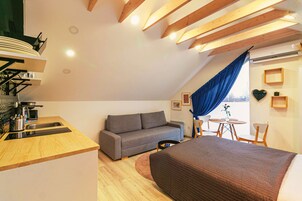 Un dormitorio tipo loft moderno con techo inclinado, un sofá, una cama, una mesa de comedor y una zona de cocina.