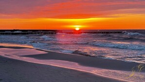 A sunset over a beach with waves and a pier in the distance. - Baltic Natur Park - Apartament B (Niechorze)