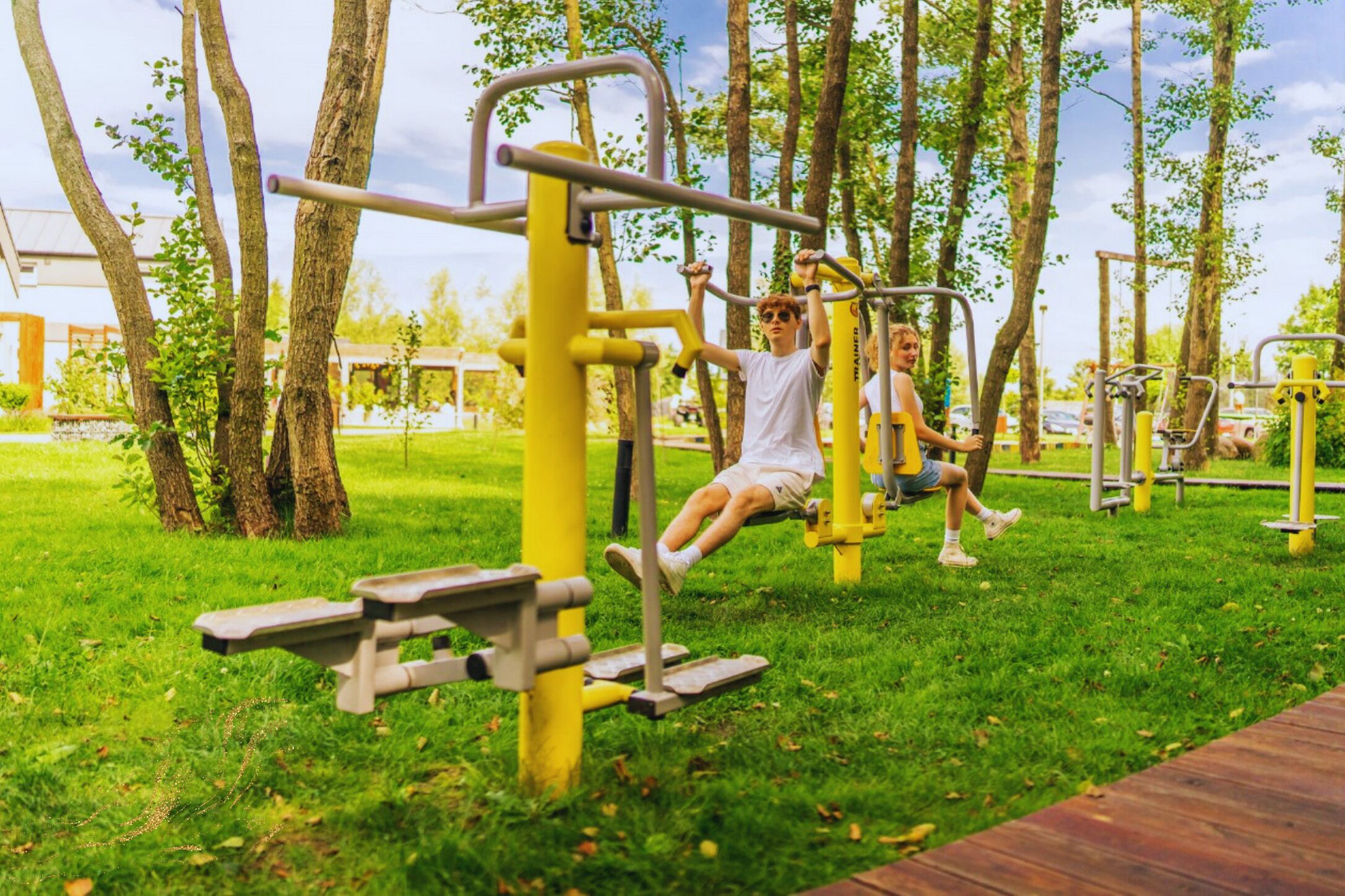 Ein Freiluft-Fitnessbereich mit Trainingsgeräten, umgeben von Bäumen und Rasen.